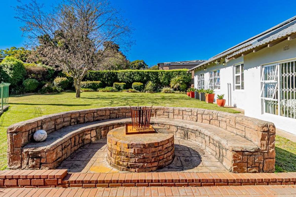 Spacious rear garden featuring a built-in brick fire pit with curved stone seating, well-maintained lawn, and established perimeter hedging.