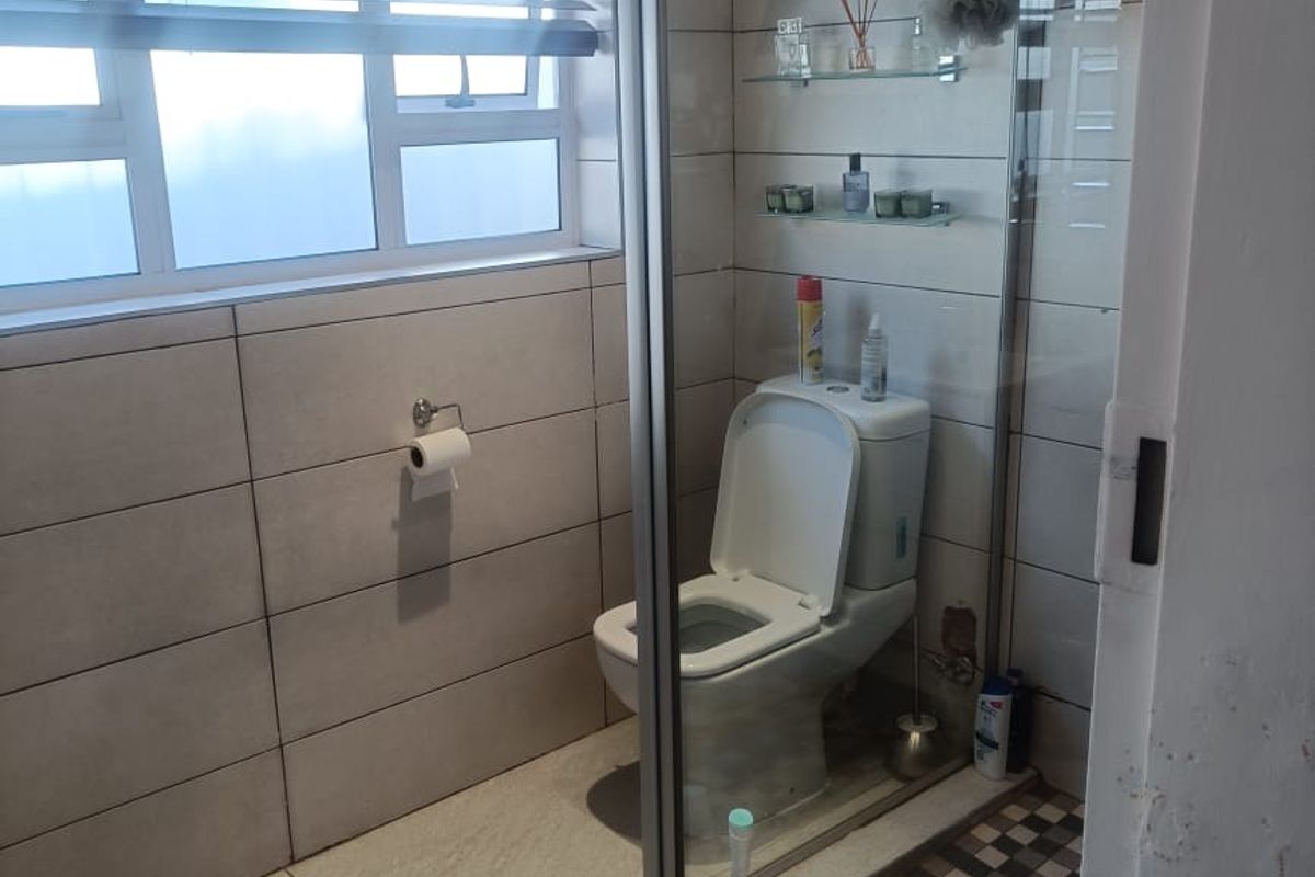 A functional bathroom featuring tiled walls and flooring, a glass-enclosed shower, and a standard toilet with integrated glass shelving.