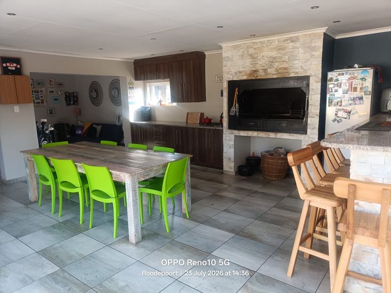 Open-plan living and dining area featuring a built-in braai with stone cladding, dark wood cabinetry, granite countertops, and tiled flooring throughout.