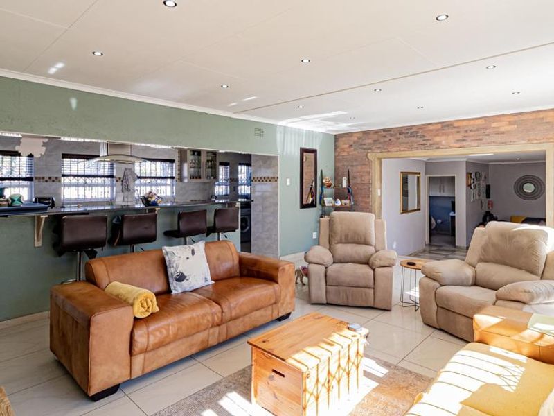 Spacious open-plan living area featuring tiled floors, recessed lighting, an exposed brick wall, and a breakfast bar overlooking the kitchen.