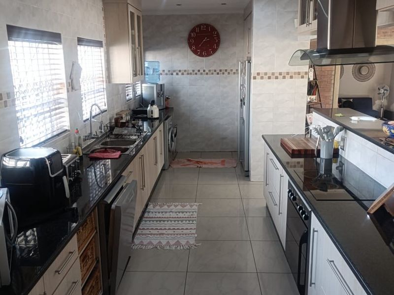 Modern galley-style kitchen featuring granite countertops, built-in oven, electric hob, stainless steel extractor fan, and ample cabinetry with tiled splashbacks.