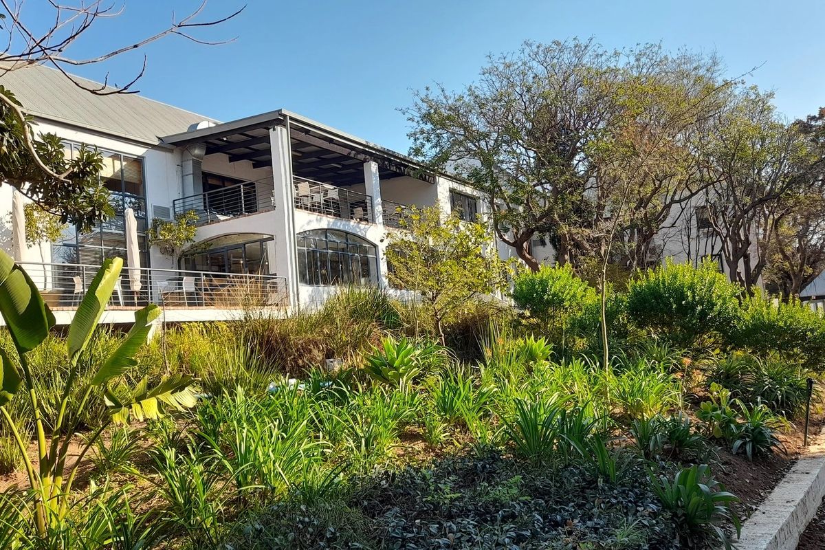 Rear view of a commercial building featuring multi-level balconies, large windows, and well-maintained landscaped gardens with paved walkways.