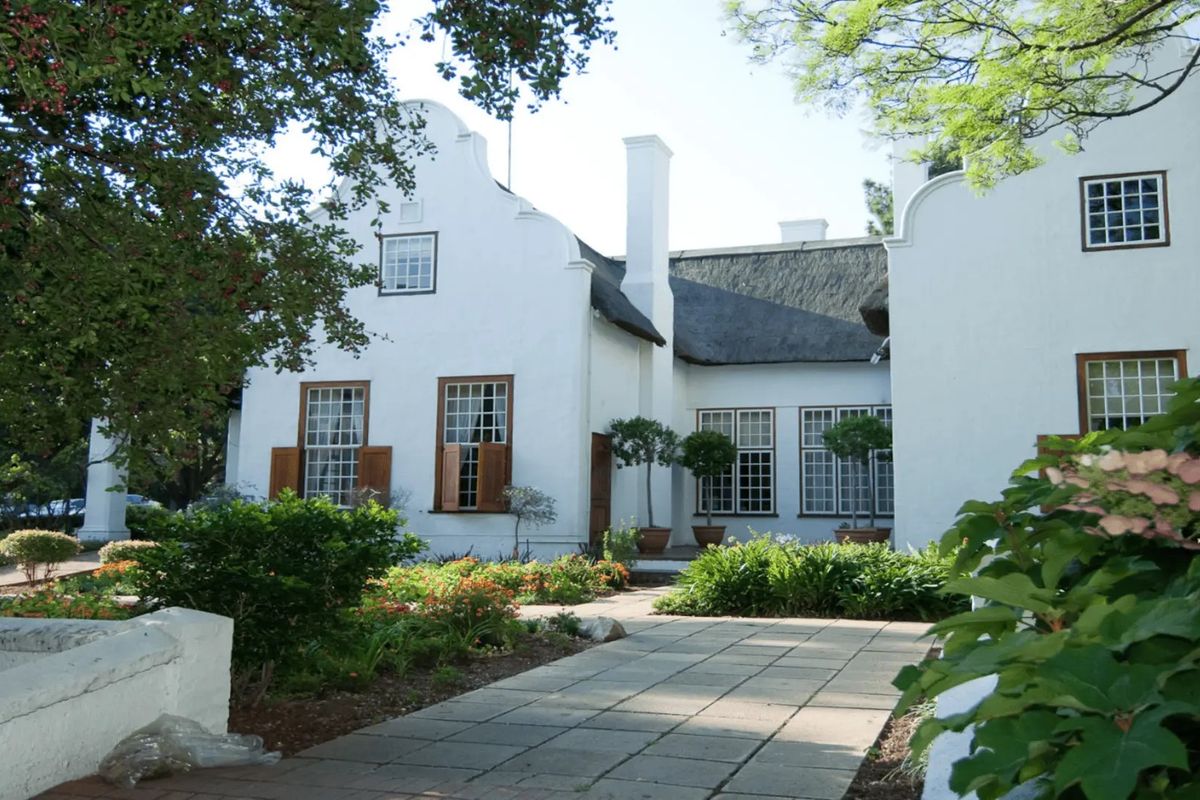A well-maintained commercial property featuring traditional Cape Dutch architecture with a thatched roof, gabled facade, and paved garden walkway.