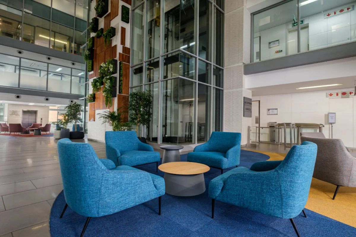 Modern commercial building lobby featuring a glass elevator shaft, vertical garden wall, and spacious open-plan reception area with high-quality finishes.