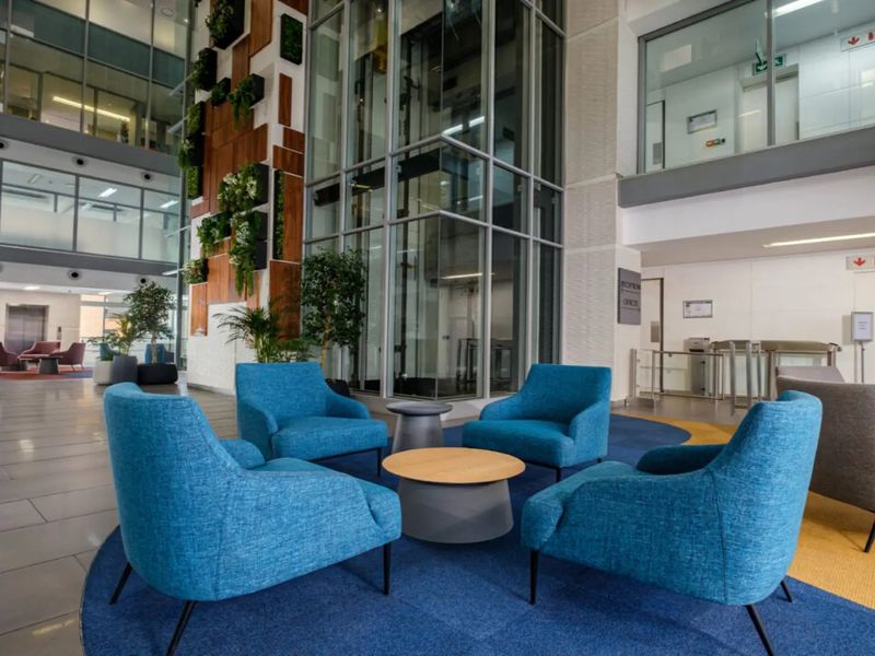 Modern commercial building lobby featuring a glass elevator shaft, vertical garden wall, and spacious open-plan reception area with high-quality finishes.