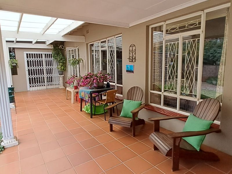 A covered outdoor patio area featuring tiled flooring, security gates, and large windows, providing a functional space for outdoor relaxation.