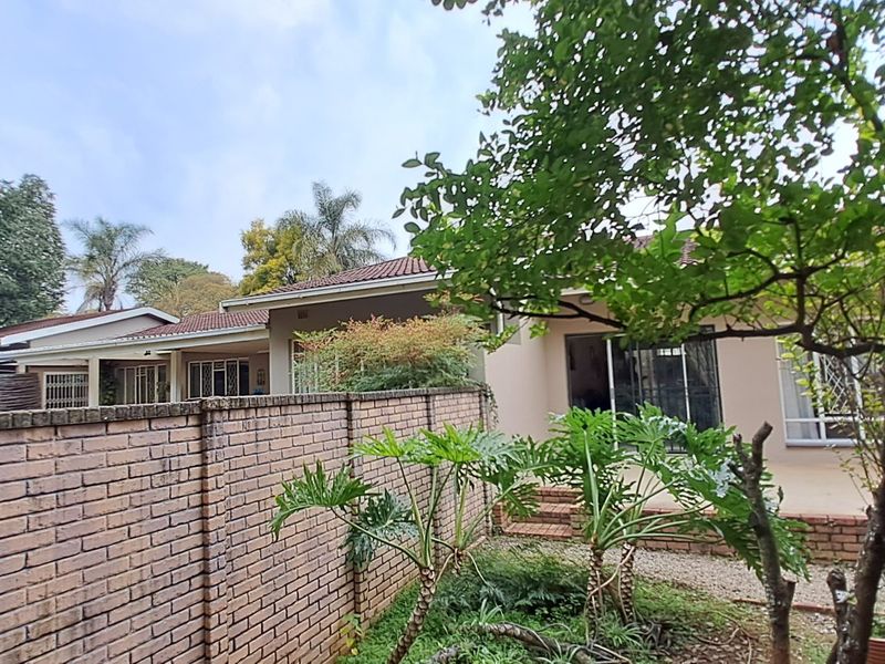 Rear view of the property featuring a paved patio area, brick boundary wall, and established garden landscaping.