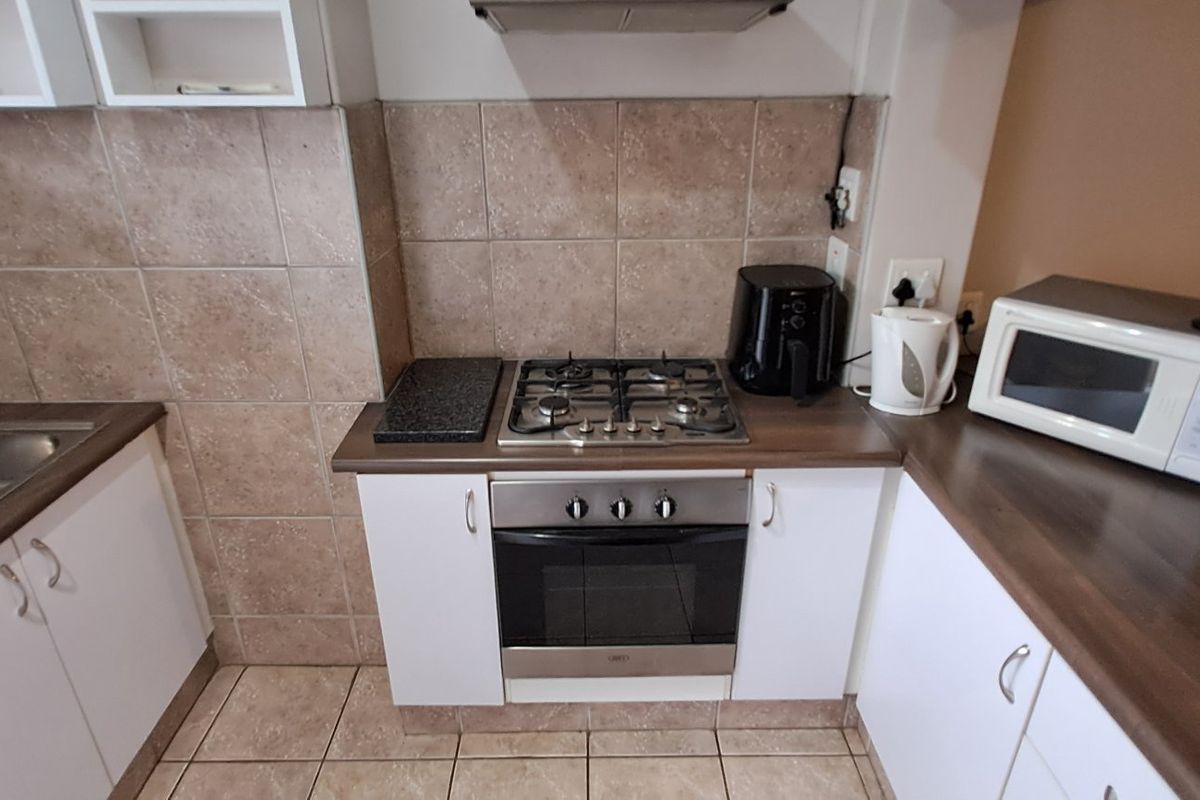 A functional kitchen featuring a gas hob, built-in oven, extractor fan, double bowl sink, and tiled splashback with ample cabinetry and counter space.