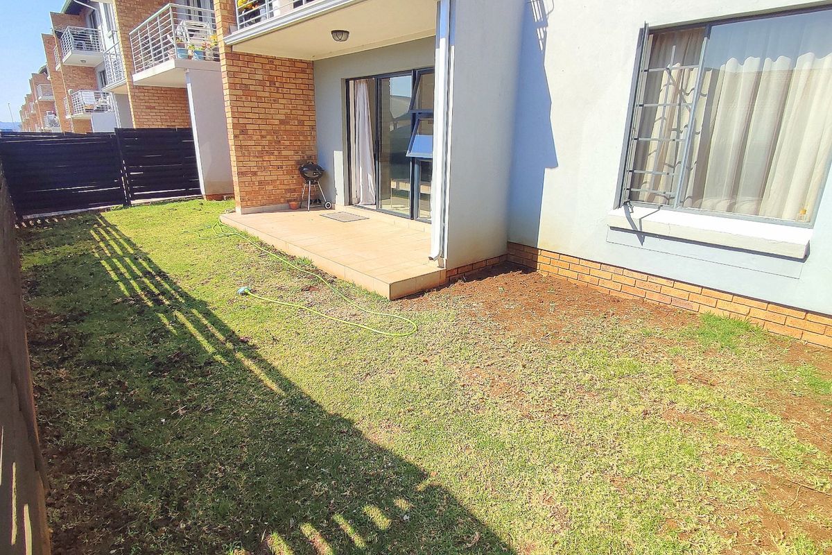 Rear view of the apartment featuring a tiled patio, brick exterior walls, security bars on windows, and a private garden area with boundary fencing.