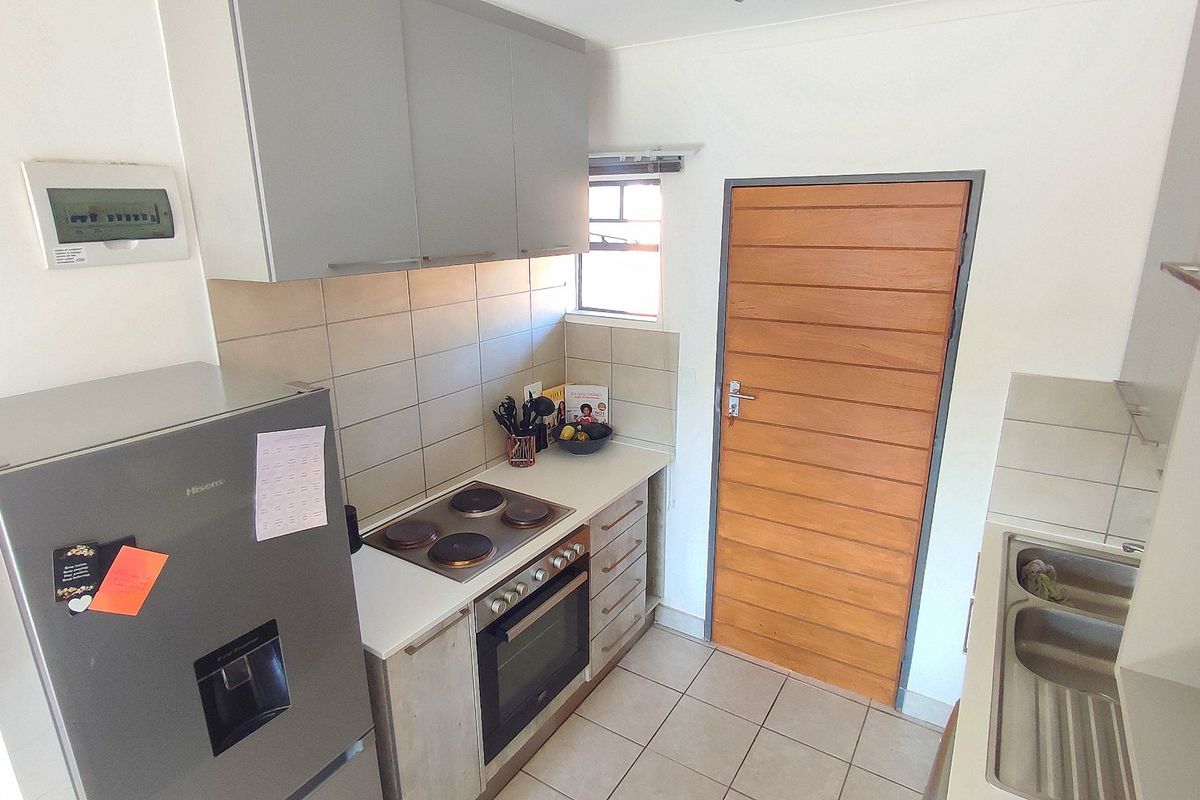 A functional kitchen featuring built-in cabinetry, an electric hob with oven, tiled backsplash, and a double stainless steel sink.