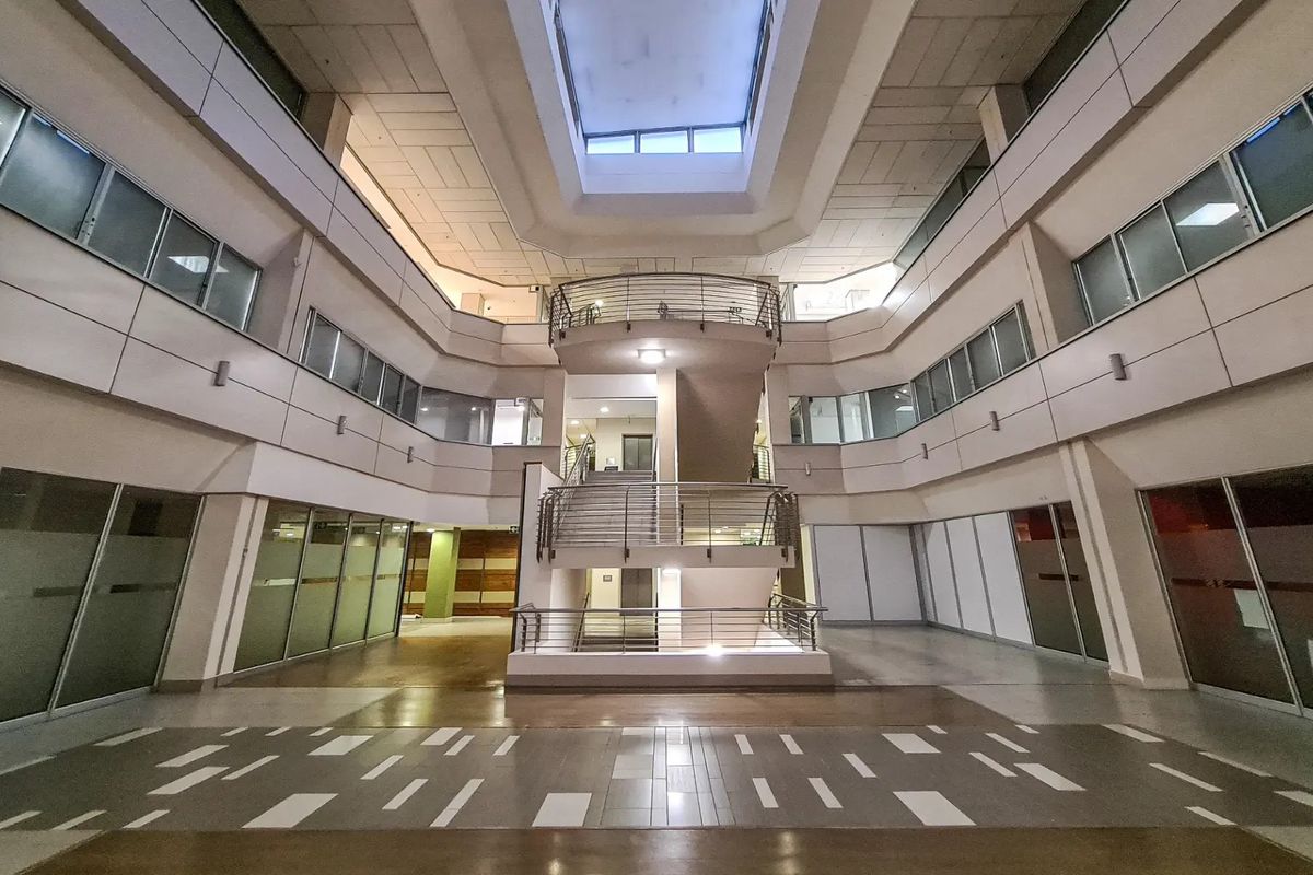 Spacious commercial atrium featuring a central staircase, multi-level glass office partitions, and a large skylight providing natural light to the open lobby area.
