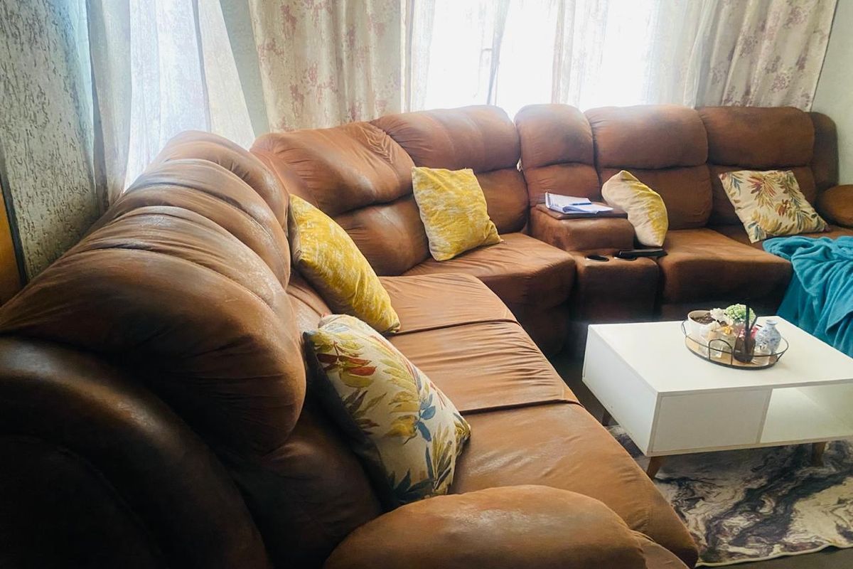 A view of a living room area featuring a large sectional sofa positioned in front of a window with curtains.