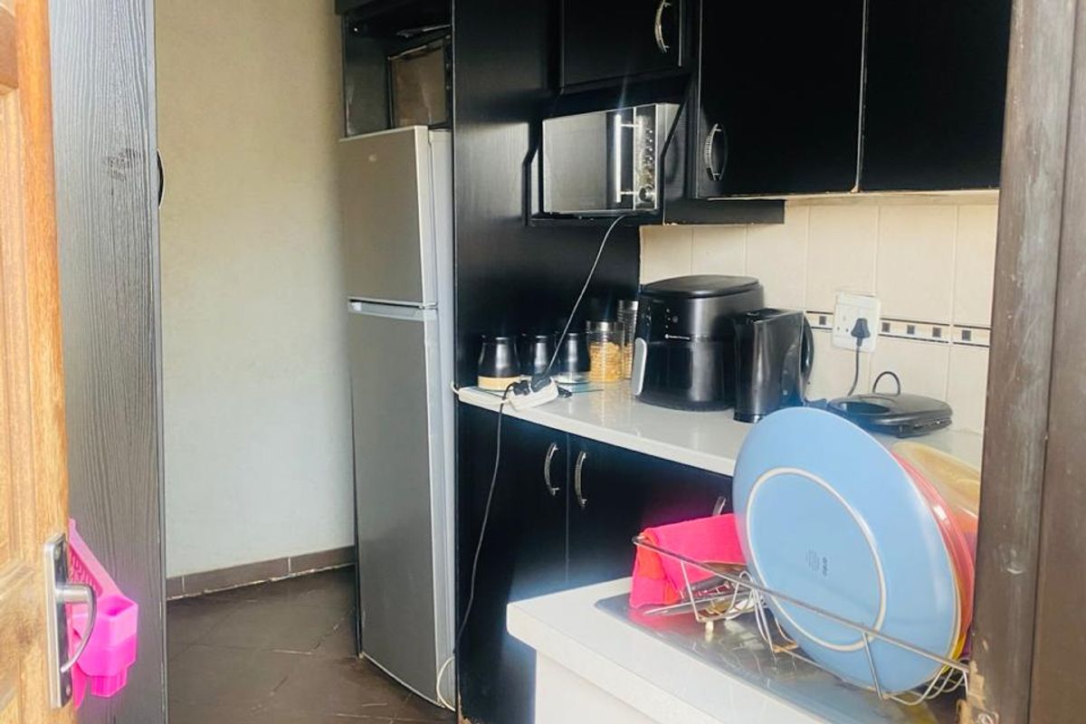 A compact kitchen featuring dark built-in cabinetry, tiled flooring, and a tiled backsplash, offering a functional layout for daily meal preparation.