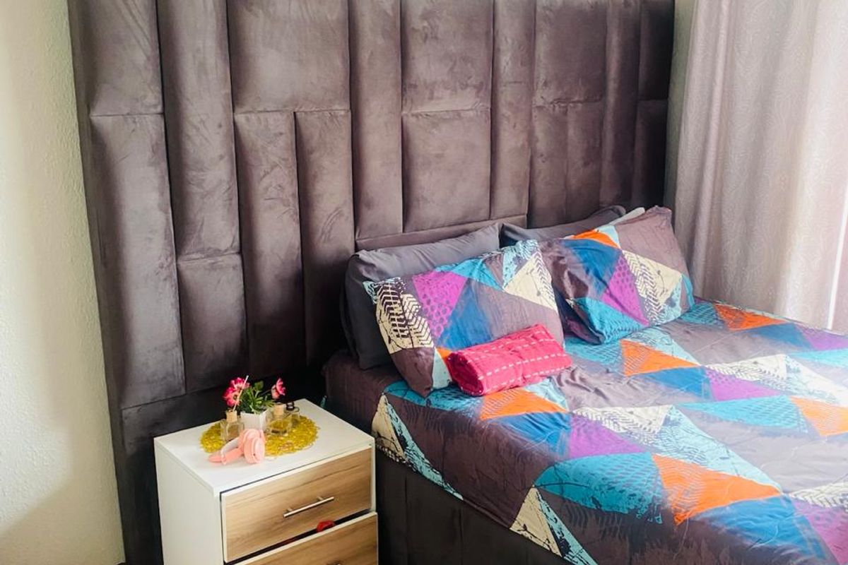 A well-maintained bedroom featuring laminate flooring and a large upholstered headboard.