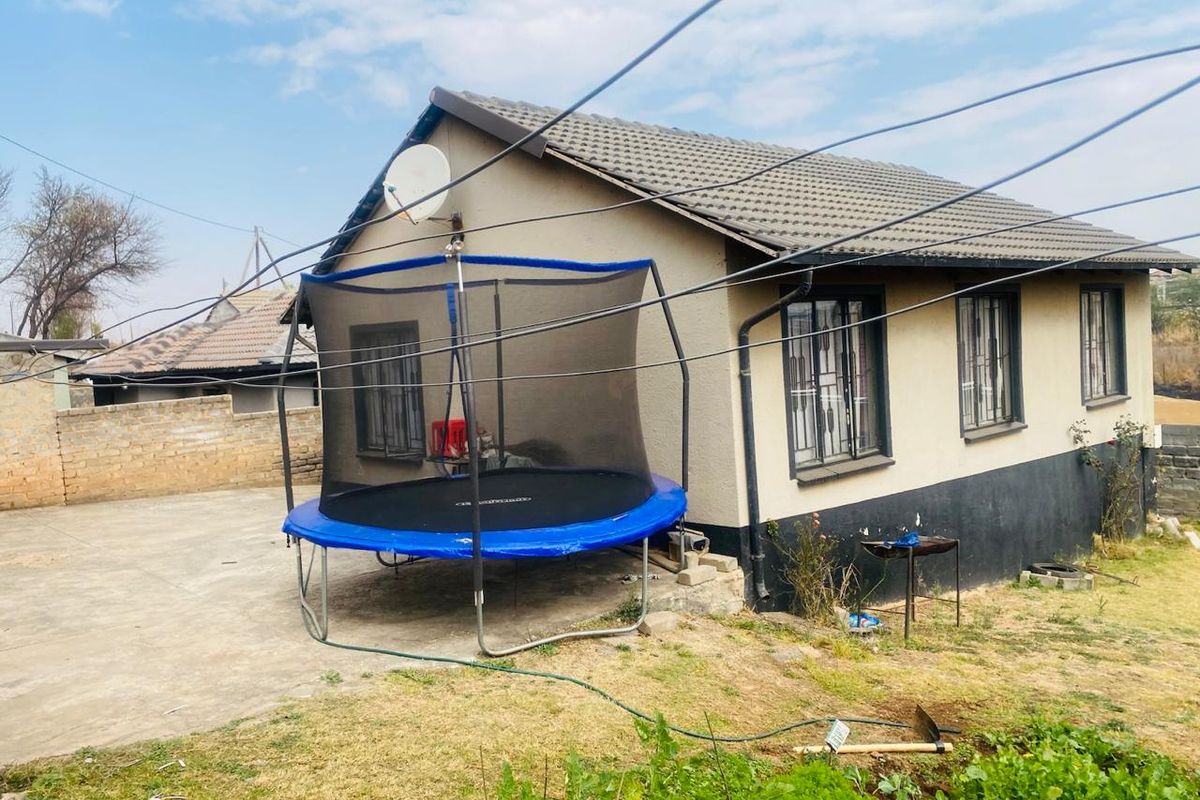 Rear view of a residential house featuring concrete roof tiles, security bars on windows, and a concrete driveway area.