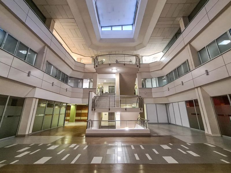 Spacious commercial atrium featuring a central staircase, multi-level glass office partitions, and a large skylight providing natural light to the open lobby area.
