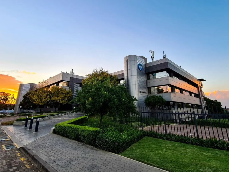 A professional exterior view of a modern multi-story commercial office building featuring glass and metal cladding, set within a well-maintained landscaped property.