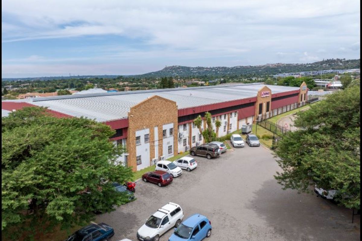 Aerial view of a commercial warehouse facility featuring a large metal roof, brick facade, and an extensive paved parking area.