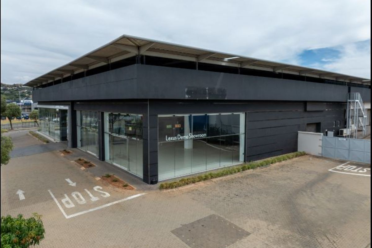 Commercial showroom building featuring large glass display windows, a metal roof structure, and an adjacent paved parking area.