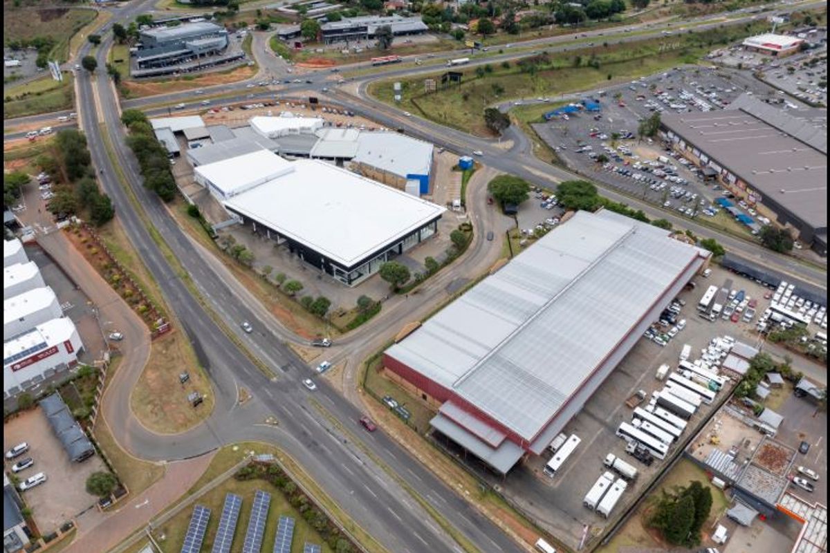 Aerial view of a commercial property complex featuring large warehouse structures, extensive parking facilities, and a solar panel installation.