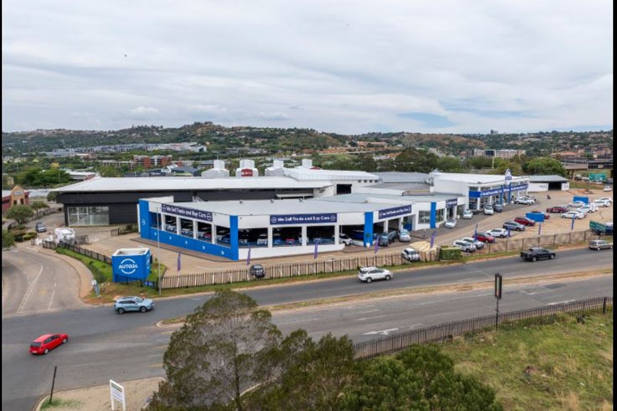 Aerial view of a commercial car dealership property featuring a large showroom, extensive parking facilities, and prominent street frontage.