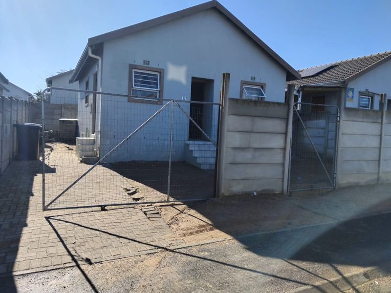 Front exterior view of a detached house featuring a paved driveway, precast concrete boundary wall, and metal gate entrance.