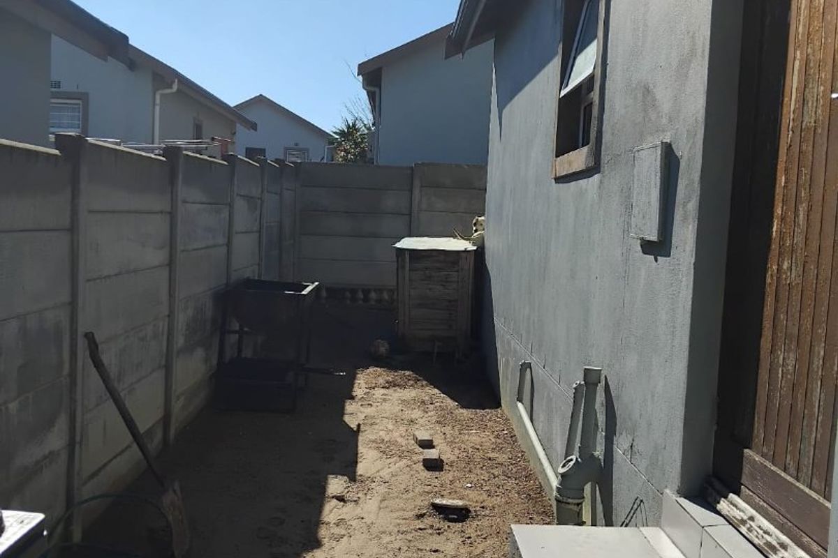 A narrow rear exterior side passage featuring a paved walkway, precast concrete boundary wall, and direct access to the home via a tiled step.