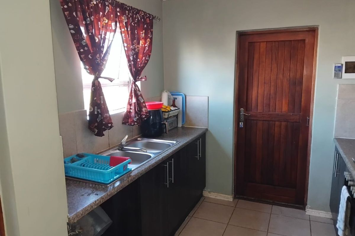 A functional kitchen area featuring dark cabinetry, a double bowl stainless steel sink, tiled flooring, and a solid wood door leading to the exterior.
