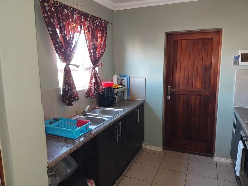 A functional kitchen area featuring dark cabinetry, a double bowl stainless steel sink, tiled flooring, and a solid wood door leading to the exterior.