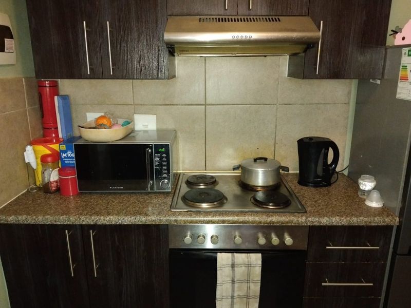 A compact kitchen area featuring dark wood cabinetry, granite countertops, a built-in oven, and an electric hob with an overhead extractor fan.