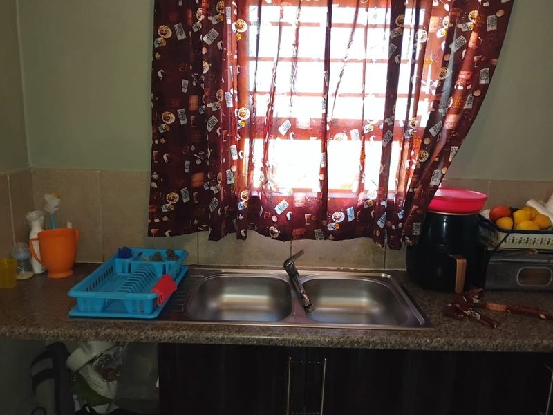 A functional kitchen sink area featuring a double bowl stainless steel sink, mixer tap, laminate countertop, and tiled splashback with built-in base cabinetry.
