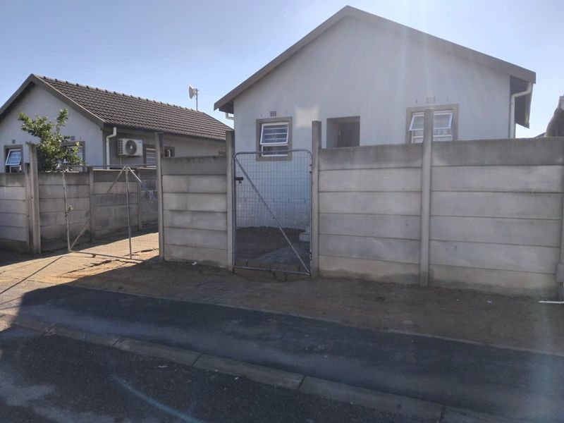 Front view of a detached house featuring a precast concrete boundary wall, metal gate, and tiled roof in a residential setting.