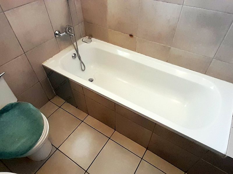 A dated bathroom featuring a built-in bathtub with shower mixer and ceramic tiling throughout, requiring cosmetic updates to improve its overall condition.