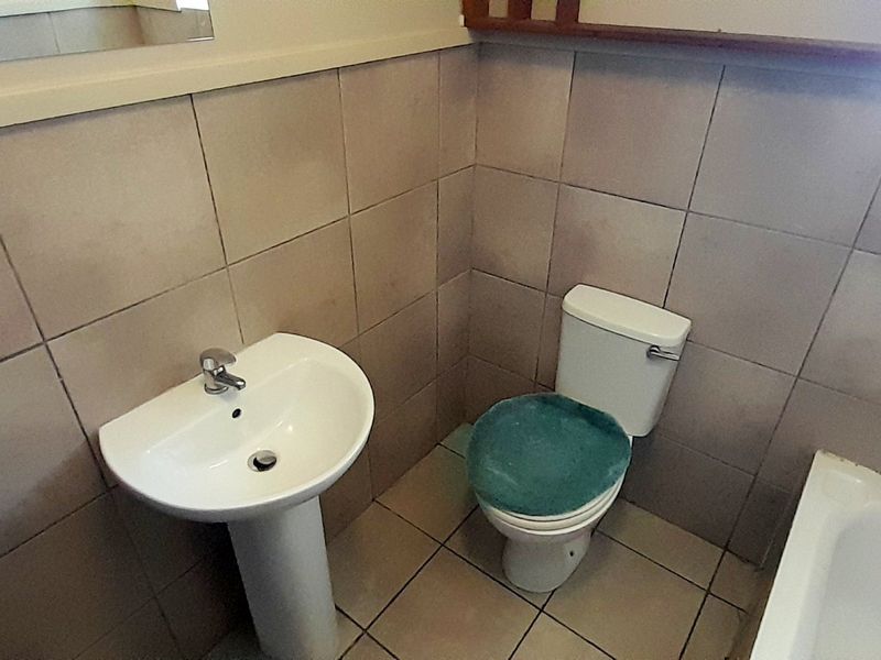 A functional bathroom featuring a pedestal basin, toilet, and bathtub with full-height wall tiling and tiled flooring.