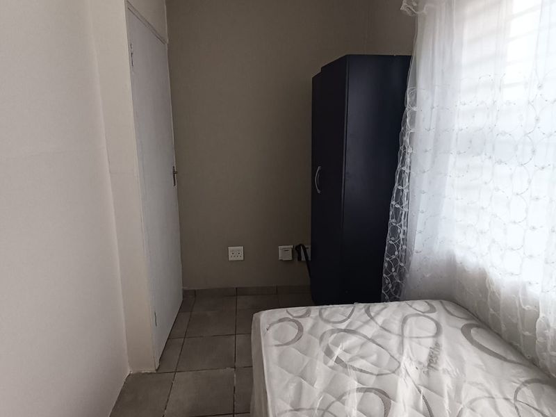 A compact bedroom featuring tiled flooring, coved ceiling details, and a window with sheer curtains.