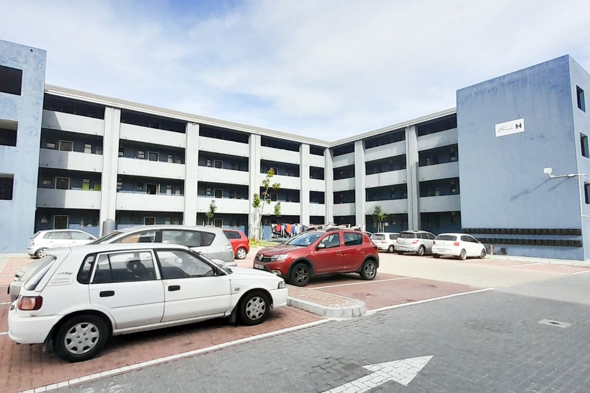 Exterior view of a multi-story residential apartment block featuring a paved parking area and communal access walkways.