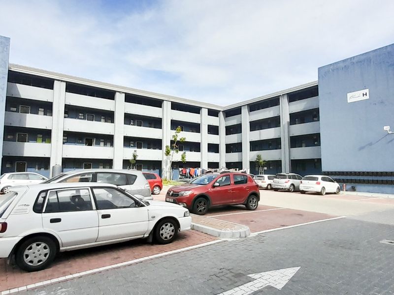 Exterior view of a multi-story residential apartment block featuring a paved parking area and communal access walkways.