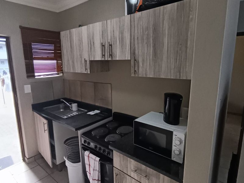 Compact kitchen featuring wood-look cabinetry, dark countertops, a stainless steel sink, and an integrated electric stove with tiled splashback.