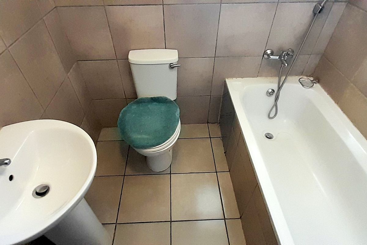 A functional bathroom featuring a pedestal basin, standard toilet, and a bathtub with wall-to-floor tiling.