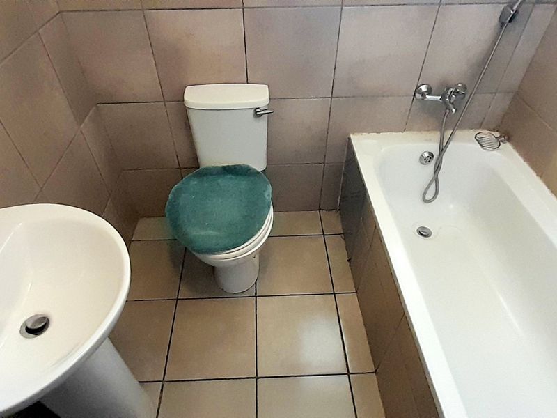 A functional bathroom featuring a pedestal basin, standard toilet, and a bathtub with wall-to-floor tiling.