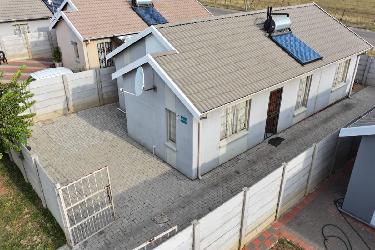 Aerial view of a residential property featuring a tiled roof with a solar water heater, paved driveway, and secure precast concrete boundary walls.