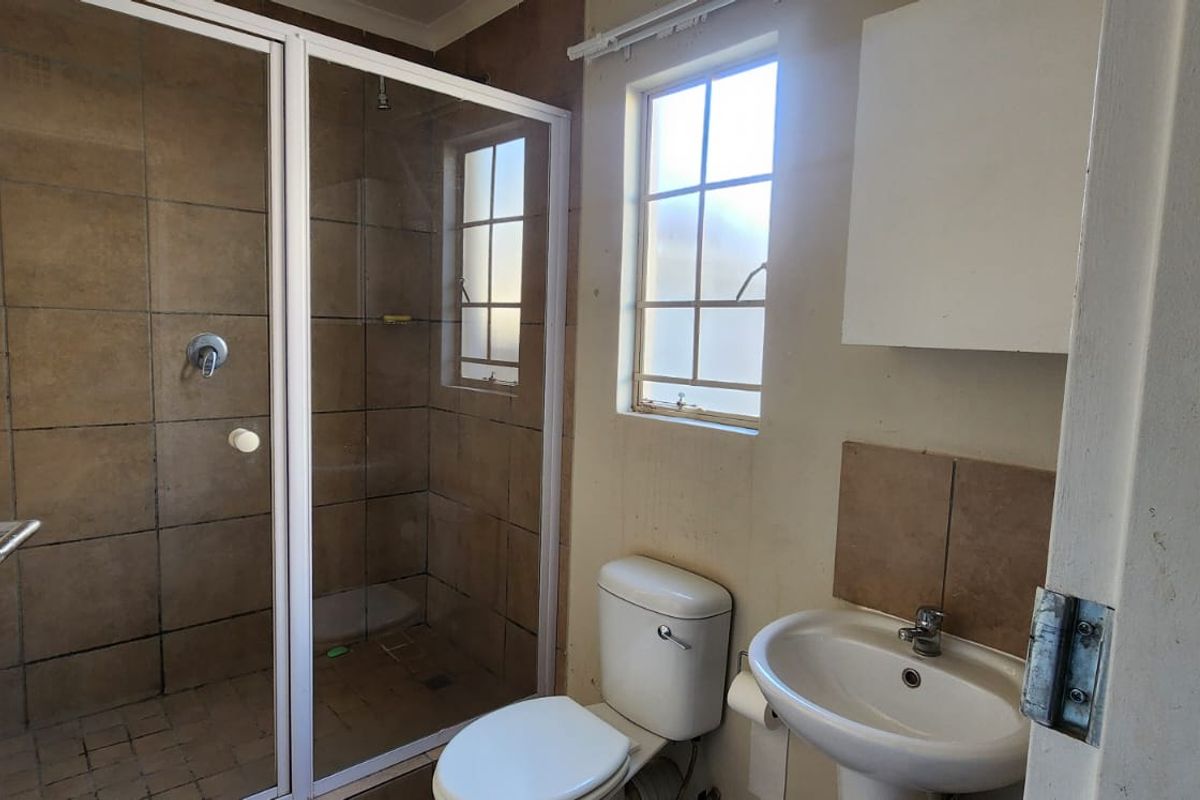 A functional bathroom featuring a shower enclosure, pedestal basin, and toilet, with neutral wall tones and natural light from the window.