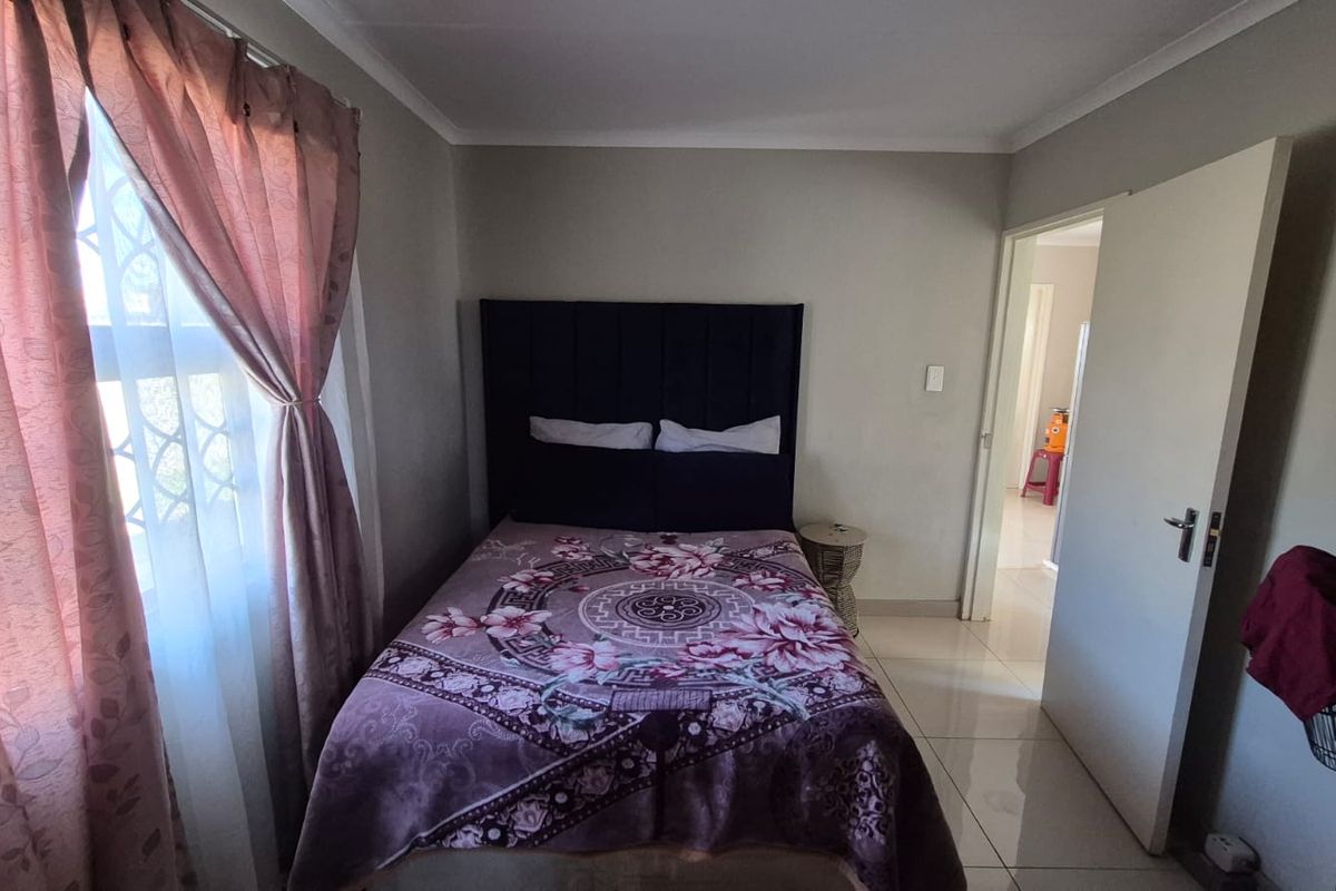 A functional bedroom featuring tiled flooring, a window with security bars, and a neutral wall finish.