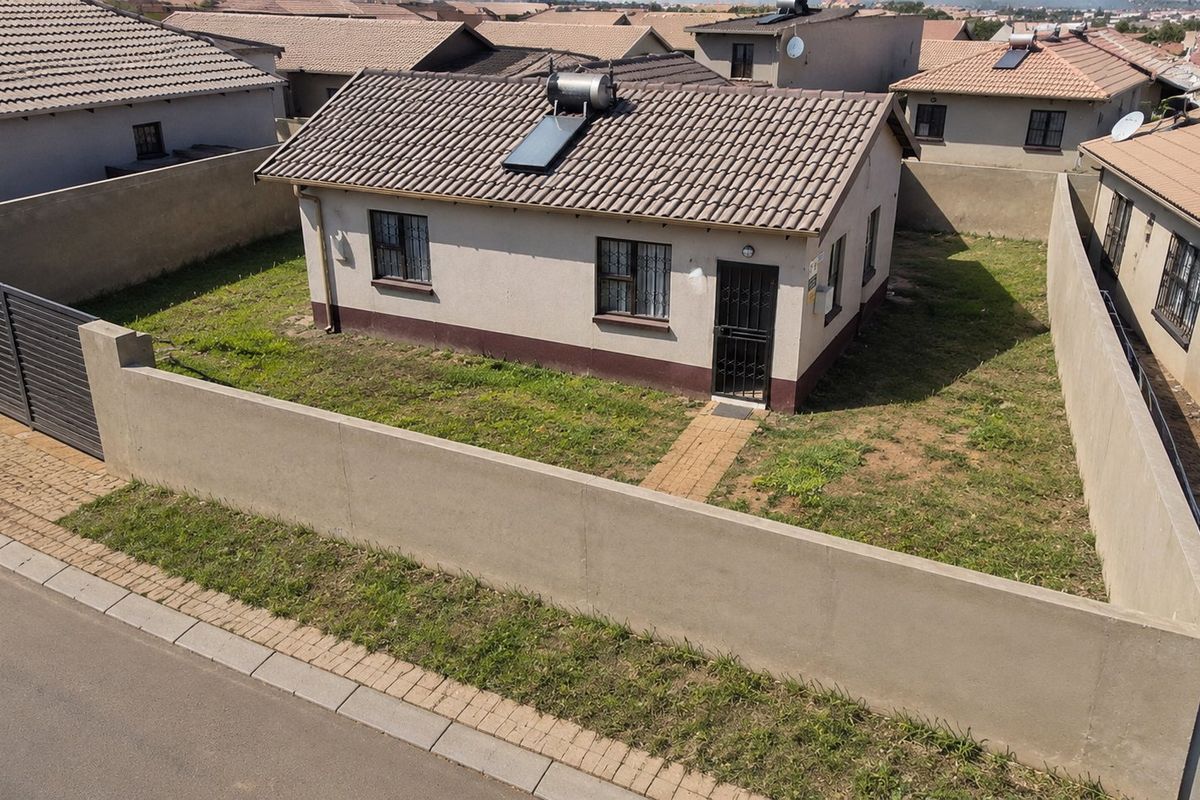 Aerial view of a detached house featuring a tiled roof with a solar water heater, enclosed by a perimeter wall with a gated entrance.