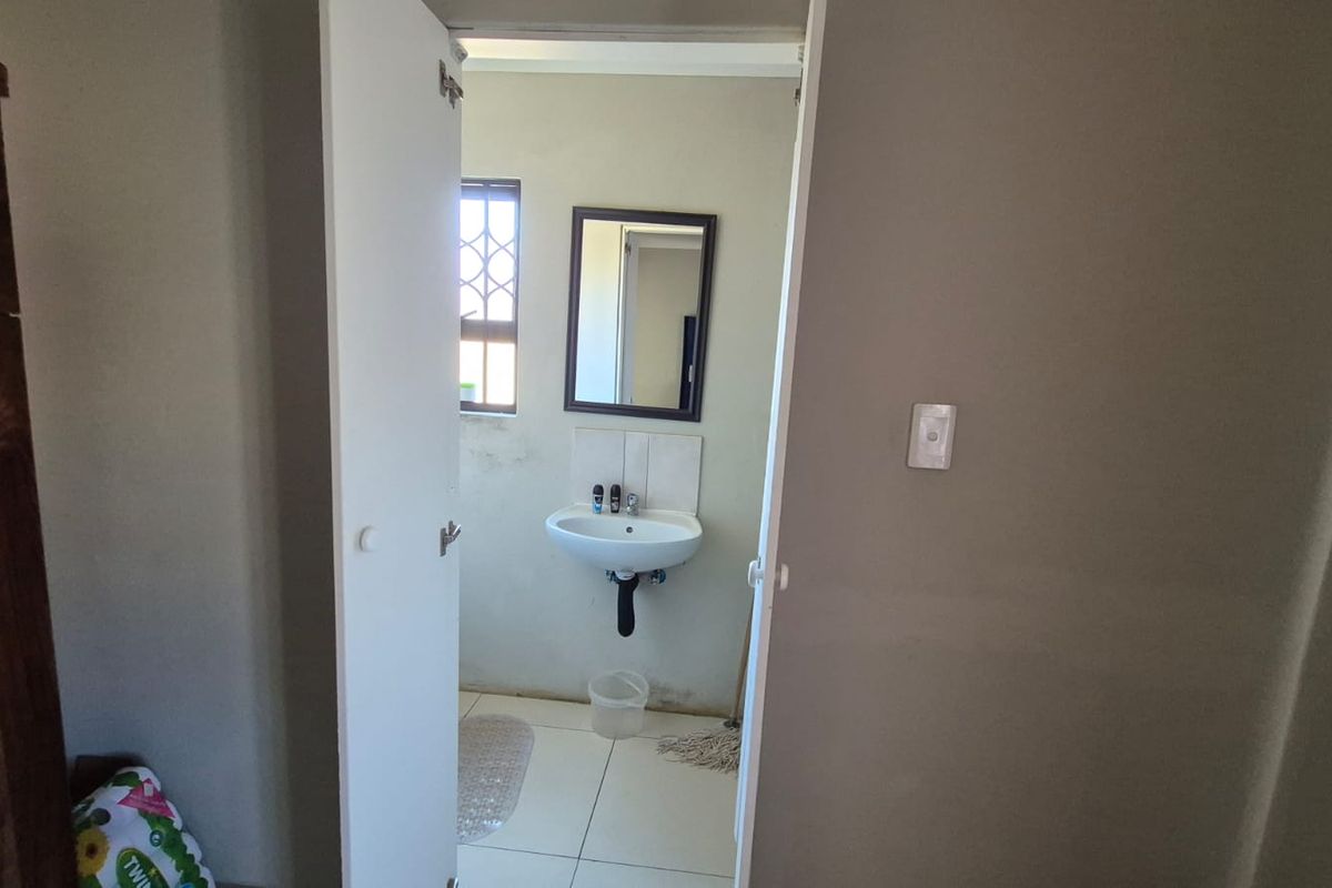 A small, functional bathroom featuring a wall-mounted basin, tiled splashback, and tiled flooring, requiring minor cosmetic updates to improve its overall appearance.