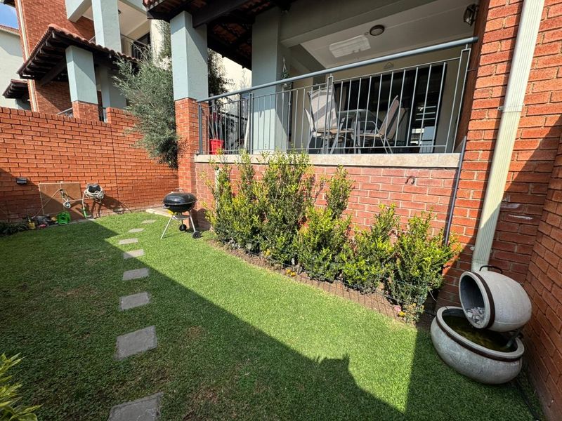 A private rear garden featuring a manicured lawn, stone water feature, and a raised patio area with metal balustrades and brick walling.