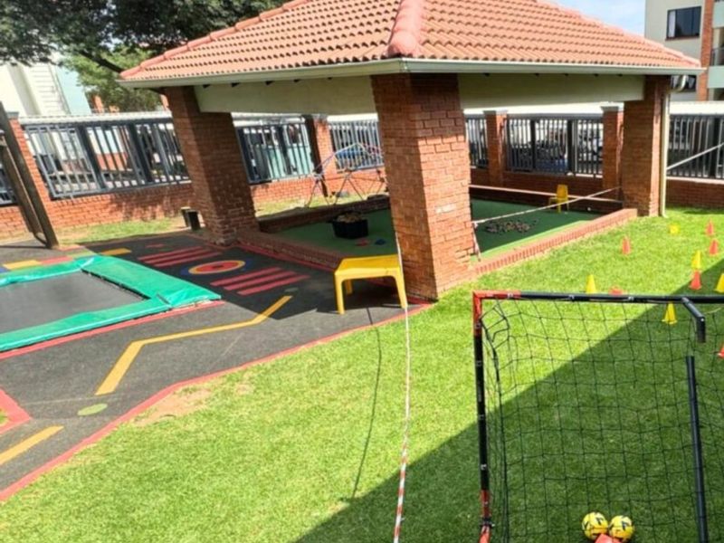 Communal garden area featuring a brick gazebo, in-ground trampoline, and lawn space, suitable for outdoor recreation within the apartment complex.