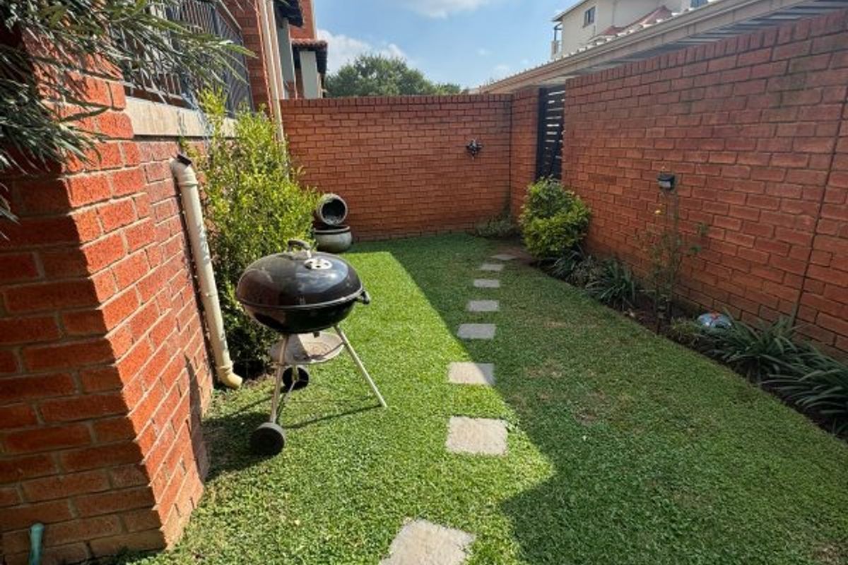 A private rear garden area featuring a brick boundary wall, a stone paver pathway, and a well-maintained lawn.