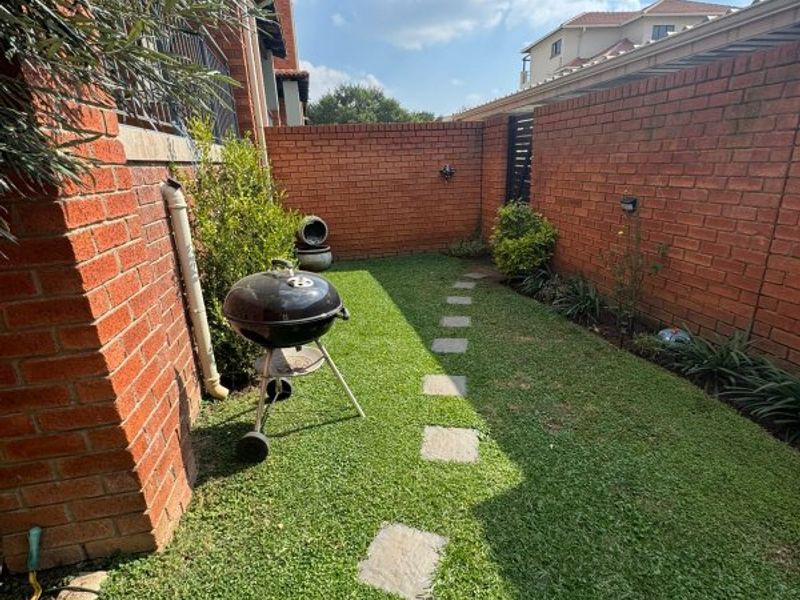 A private rear garden area featuring a brick boundary wall, a stone paver pathway, and a well-maintained lawn.