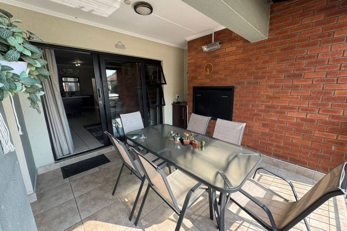 A covered patio area featuring tiled flooring, an exposed brick wall, and a built-in braai, providing a functional outdoor entertainment space.